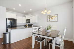 Kitchen with dark stone counters, white cabinets, a chandelier, black appliances, and dark wood finished floors