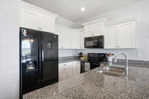 Kitchen with black appliances, white cabinetry, dark stone counters, and recessed lighting