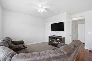 Living area featuring a ceiling fan, a glass covered fireplace, and dark colored carpet