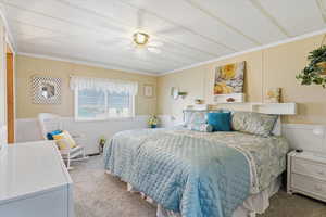 Bedroom with a wainscoted wall, a decorative wall, carpet flooring, crown molding, and a ceiling fan