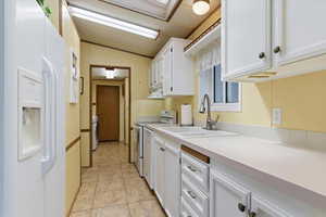 Kitchen featuring white appliances, white cabinetry, lofted ceiling, light countertops, and light tile patterned flooring