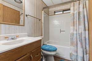 Full bathroom featuring vanity, shower / bathtub combination with curtain, and wood walls