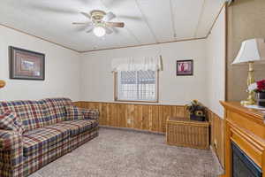 Carpeted living room with wooden walls, a wainscoted wall, ceiling fan, and a textured ceiling