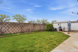 Fenced backyard featuring a storage unit and a patio area