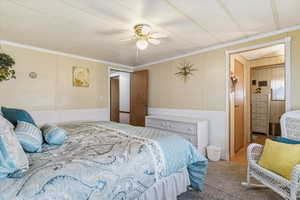 Carpeted bedroom featuring ornamental molding, wainscoting, ceiling fan, and a decorative wall