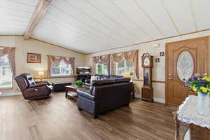 Living room with dark wood-style floors, healthy amount of natural light, and vaulted ceiling with beams