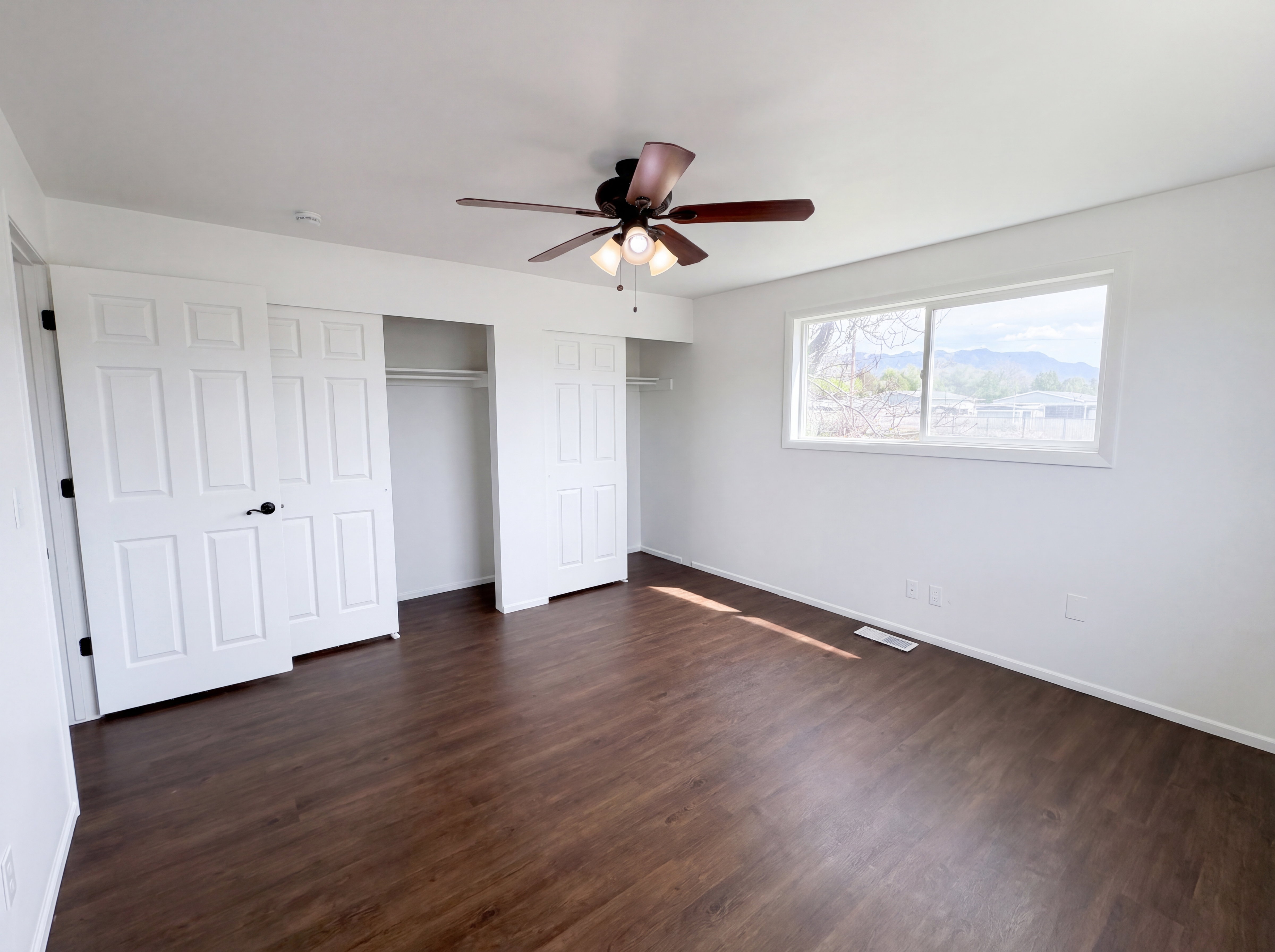 Unfurnished bedroom with dark wood-style floors, multiple closets, and ceiling fan