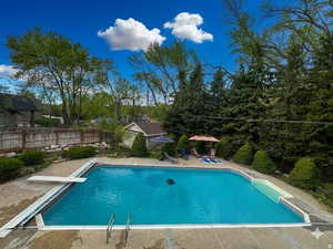 View of pool featuring patio surround, a diving board, view of wooded area, and a fenced backyard