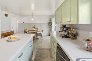 Kitchen featuring green cabinetry, dishwasher, light countertops, and hanging light fixtures