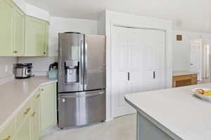 Kitchen featuring stainless steel refrigerator with ice dispenser, green cabinetry, and light countertops