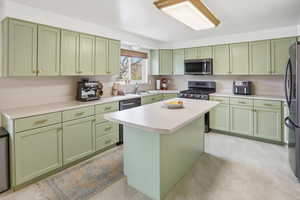 Kitchen with green cabinets, stainless steel appliances, light countertops, and a kitchen island