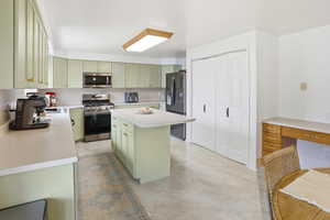 Kitchen with green cabinets, finished concrete flooring, stainless steel appliances, a center island, and light countertops