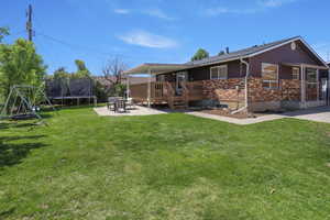 Rear view of house with a deck, a trampoline, a lawn, and brick siding