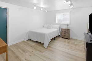 Bedroom featuring light wood-type flooring, track lighting, and a textured ceiling