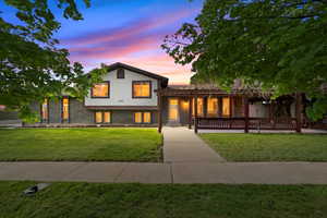 Stunning twilight view showcasing the home’s inviting curb appeal with warm interior lighting, mature trees, and charming covered front porch.