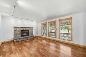 Bright and open living room featuring beautiful hardwood floors, large front windows, and a stunning stone fireplace.