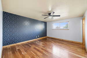 Spacious primary bedroom with hardwood flooring, ceiling fan, and stylish accent wall.