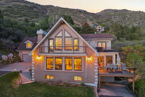 Back of house at dusk featuring a balcony, a chimney, brick siding, driveway, and a garage