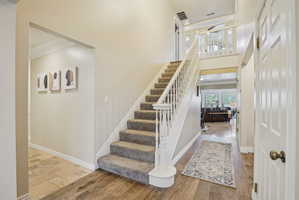 Stairs featuring crown molding, wood finished floors, and a high ceiling