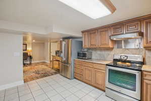 Kitchen featuring stainless steel appliances, light tile patterned flooring, wood finish cabinetry, and decorative backsplash