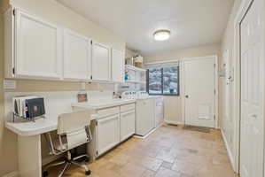 Laundry area featuring stone tile floors, washing machine and dryer, an office area, and cabinet space