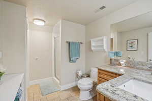 Full bath with vanity, a shower stall, light stone finish floors, and a textured ceiling