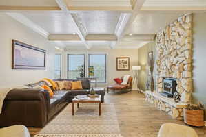 Living room featuring light wood-style floors, a wood stove, crown molding, and coffered ceiling