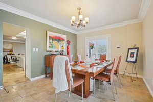 Dining area featuring stone tile flooring, crown molding, and a chandelier
