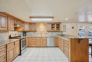 Kitchen with a peninsula, a breakfast bar, stainless steel appliances, glass fronted cabinets, and wood finish cabinets