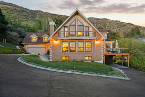 View of front of property featuring driveway, brick siding, a chimney, a mountain view, and a balcony