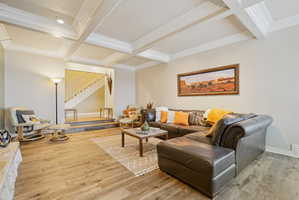 Living room with coffered ceiling, light wood-style floors, and ornamental molding