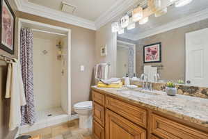 Bathroom featuring a stall shower, crown molding, vanity, and stone tile floors
