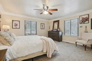 Bedroom featuring ornamental molding, multiple windows, light carpet, a textured ceiling, and ceiling fan