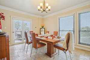Dining space featuring stone tile floors, a chandelier, and ornamental molding