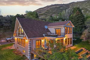 Back of property at dusk with a balcony, a shingled roof, a mountain view, and brick siding