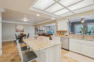 Kitchen featuring a breakfast bar, ornamental molding, stone tile floors, a kitchen island, and stainless steel dishwasher