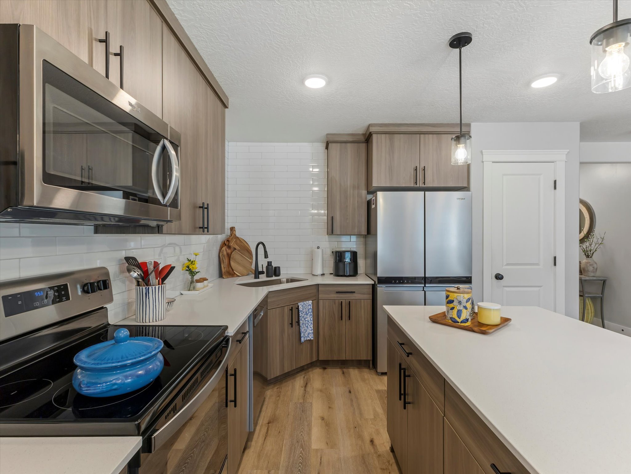 Kitchen featuring stainless steel appliances, light wood finished floors, decorative backsplash, decorative light fixtures, and wood finish cabinetry