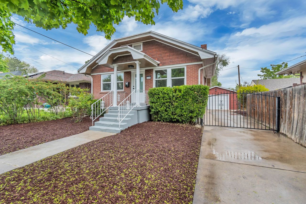 Bungalow-style home with a chimney, brick siding, a gate, and an outbuilding