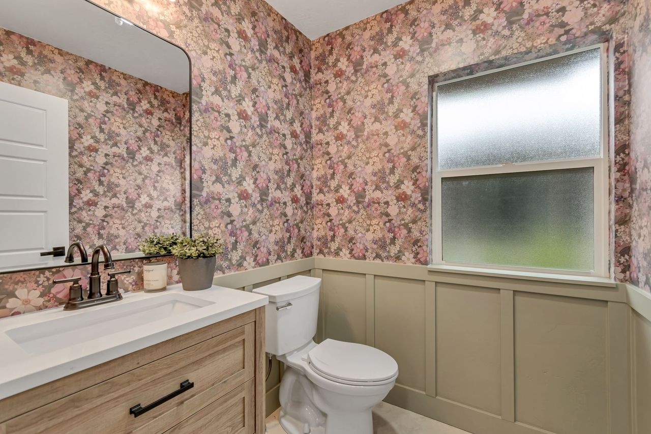 Half bathroom featuring vanity, wainscoting, a decorative wall, and wallpapered walls