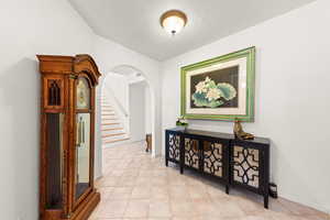 Hall with arched walkways, light tile patterned flooring, and a textured ceiling