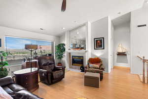 Living room with a tiled fireplace, light wood-style floors, a ceiling fan, and vaulted ceiling