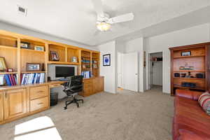 Home office featuring light colored carpet, ceiling fan, built in desk, and a textured ceiling