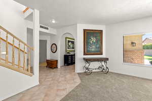 Entryway with arched walkways, light tile patterned floors, a textured ceiling, and light colored carpet