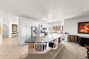 Kitchen featuring arched walkways, a breakfast bar, glass insert cabinets, stainless steel appliances, and white cabinets