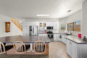 Kitchen featuring a breakfast bar, dark stone countertops, stainless steel appliances, white cabinets, and glass insert cabinets