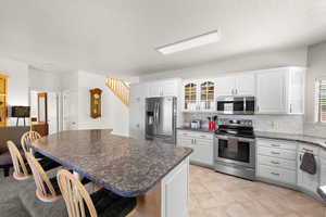 Kitchen featuring stainless steel appliances, a breakfast bar, white cabinets, backsplash, and glass fronted cabinets