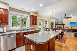 Kitchen with stainless steel dishwasher, open floor plan, a kitchen island, light stone counters, and lofted ceiling