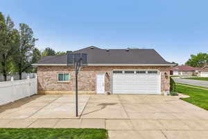 View of property exterior featuring a patio, brick siding, roof with shingles, driveway, and a garage
