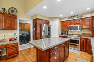 Kitchen with washer and clothes dryer, stainless steel appliances, a center island, light stone counters, and light wood-style floors