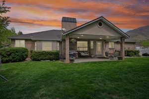 Back of property at dusk featuring a patio area, a yard, brick siding, and a chimney